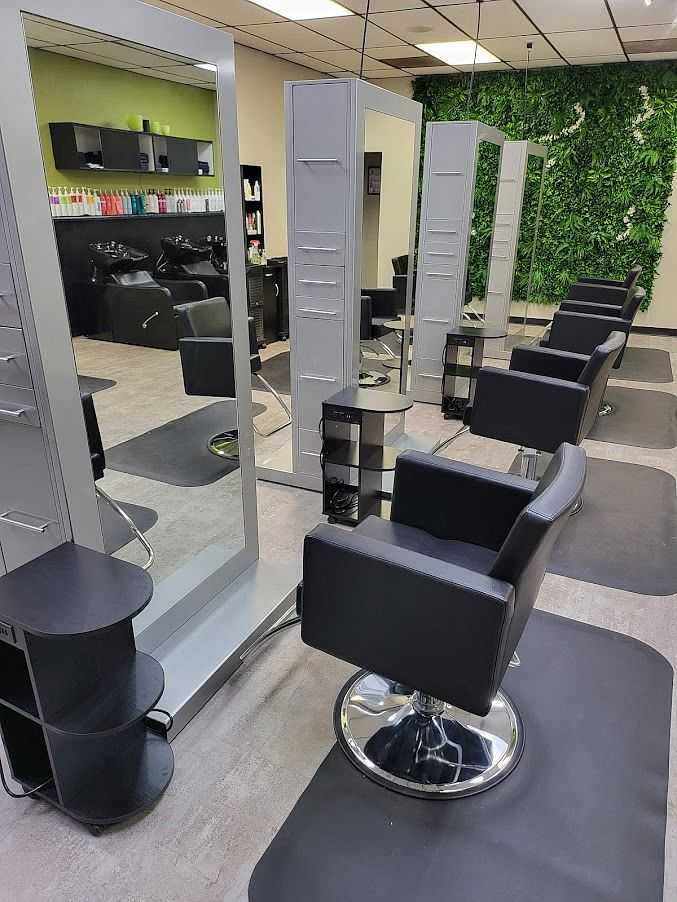 Modern salon with black chairs, large mirrors, and green wall plants in well-lit, chic setting.