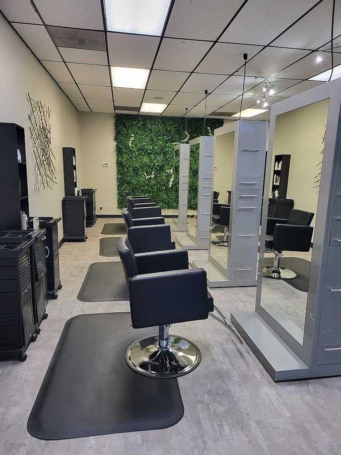 Modern hair salon with black chairs, mirrors, and a green plant wall in the background.