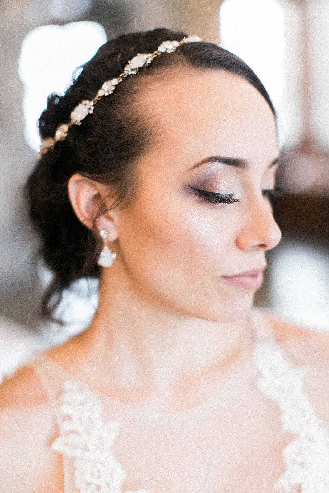 Bride with pearl headband and lace dress looking down, with soft focus background.