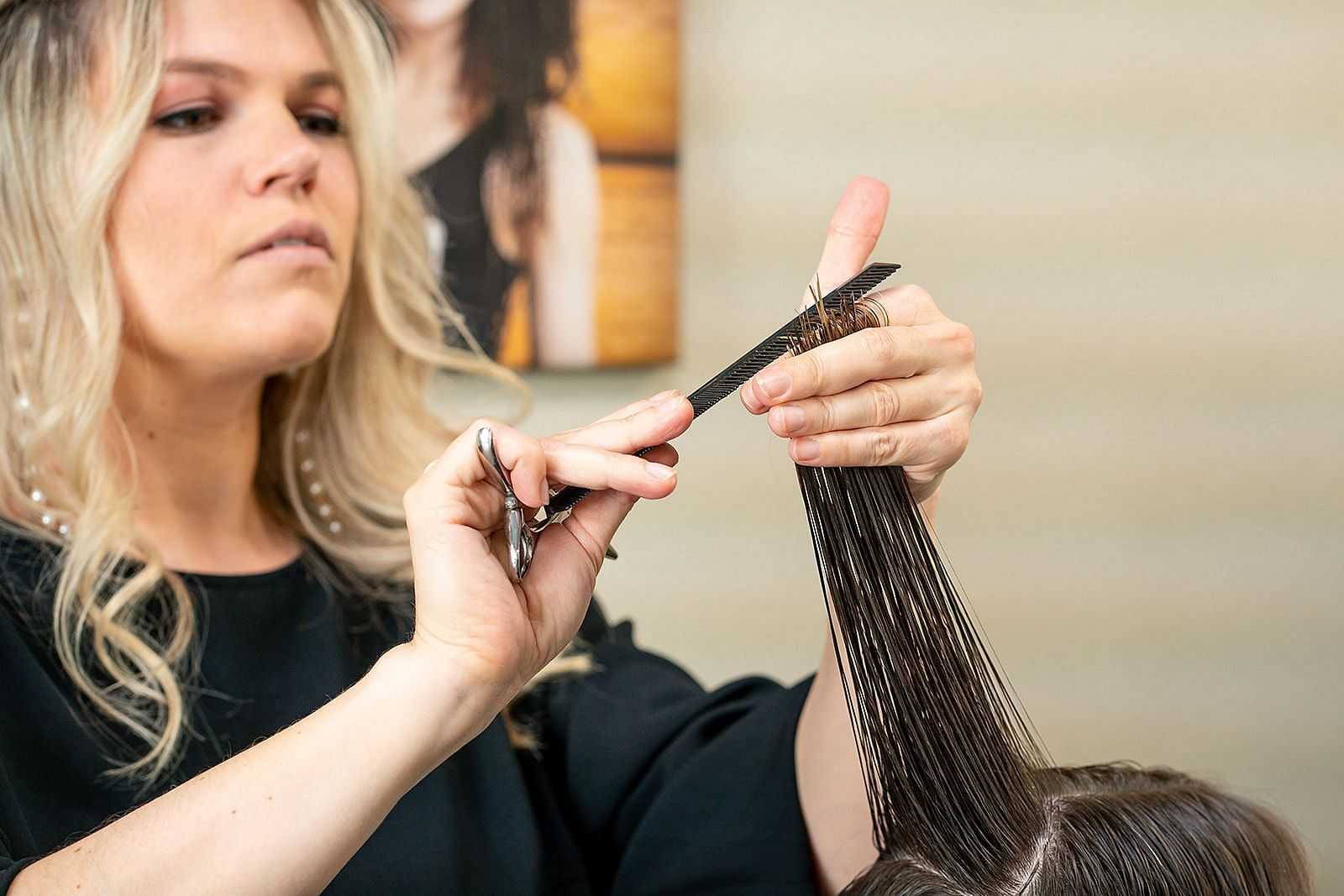 Hairstylist precisely trimming a client's hair with scissors and comb in a salon.